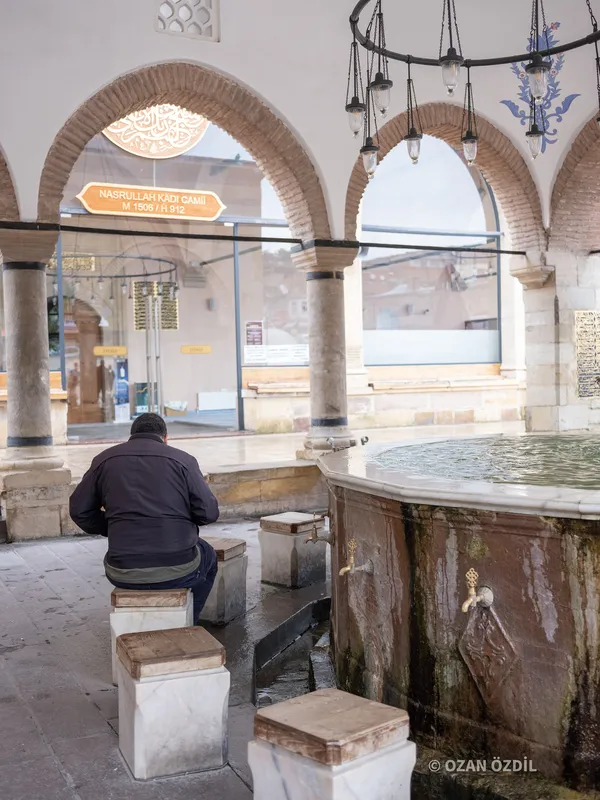 Şadırvan revakı altında oturan bir adam.